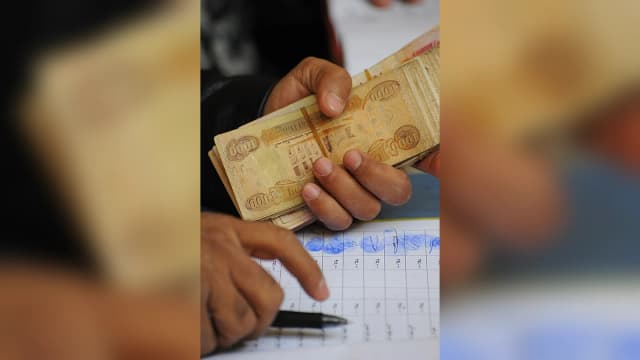 يد تحمل رزمة من الدنانير العراقية فوق سجل لصرف الرواتب خلال عملية دفع في بغداد عام 2009.